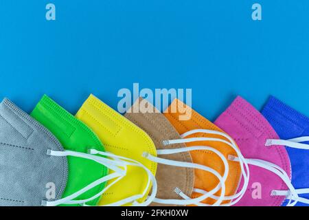 stack of  different colors FFP2 or N95 face masks respirators without exhalation valve on blue background. Top view flat layer. Protection from covid Stock Photo