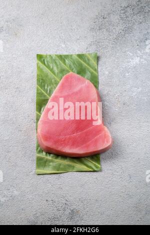 Raw tuna steak on green leaf, grey background Stock Photo