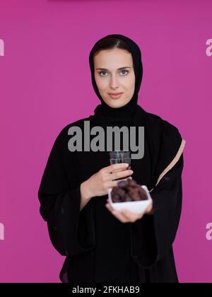 Modern Muslim woman in abaya holding a date fruit and glass of water in front of her. Concept celebration of iftar time, end of fasting, in Ramadan ho Stock Photo