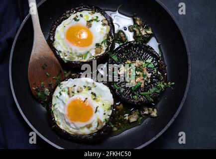 A pan with fried eggs and portobello mushrooms on dark background. Directly above. Stock Photo