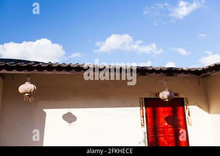 Sunrise shining on an old Yunnanese house, red door against white wall and blue sky in the backgrounds. Doi Mae Salong, Chiang Rai, Thailand. Stock Photo