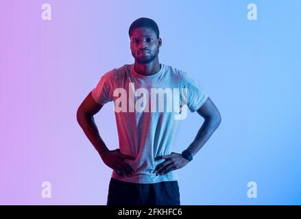 African American male fitness model standing with arms on hips, looking at camera in neon lighting Stock Photo