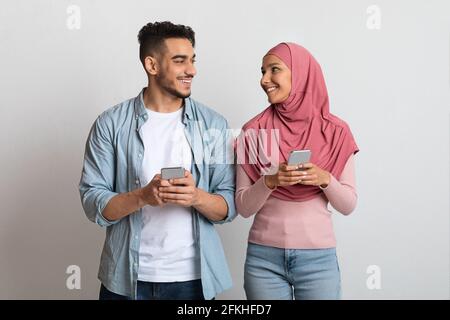 Muslim Dating Apps. Portrait Of Happy Islamic Couple With Smartphones In Hands Stock Photo