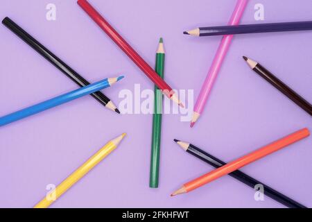 Colored pencils are scattered in a chaotic manner on a lilac background. Stock Photo