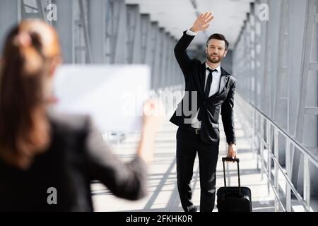 Cheerful businessman waving to assistance, meeting in airport Stock Photo