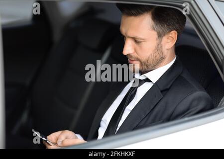 Wealthy manager sitting in car and using smartphone Stock Photo
