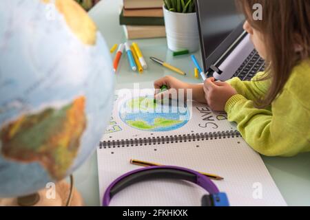 Wide angle view of child girl draws planet earth with wax colors on school notebook for Earth day - Little activist girl writes the message for future Stock Photo