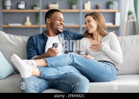 Romantic Young Multiracial Couple Relaxing On Couch And Chatting Together Stock Photo