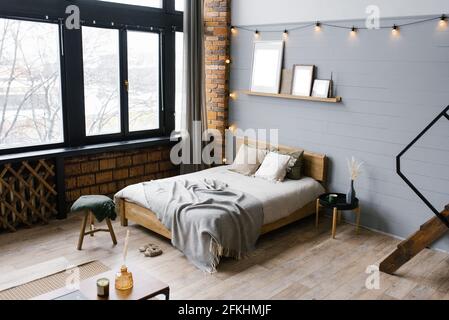 The interior of the bedroom is in a modern Scandinavian style with gray wooden and brick walls, a comfortable double bed, a panoramic window Stock Photo