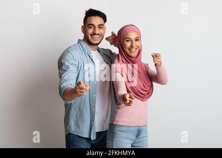 Cheerful Islamic Spouses Pointing Fingers At Camera, Indicating Somebody. Stock Photo
