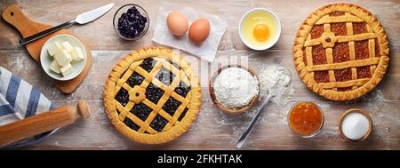 Two tarts, shortcrust pastry with sour cherry and orange jam, flour, butter, eggs and other ingredients on pastry board. Top view, flat lay. Stock Photo