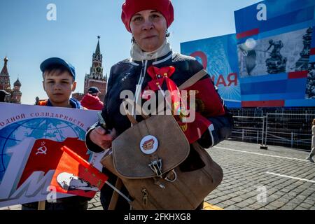 Moscow, Russia. 1st of May, 2021 People walk on Red Square in Moscow during the holiday of Labour Day, also knows as May Day, on the background of a poster decorated for the Victory Day (9th May). In 2021, in Moscow, the city authorities decided to cancel the May Day traditional demonstration due to the difficult epidemiological situation with the novel coronavirus COVID-19 disease in the region. The inscription on the banner reads 'The 1st May. The International Workers' Solidarity Day' Stock Photo