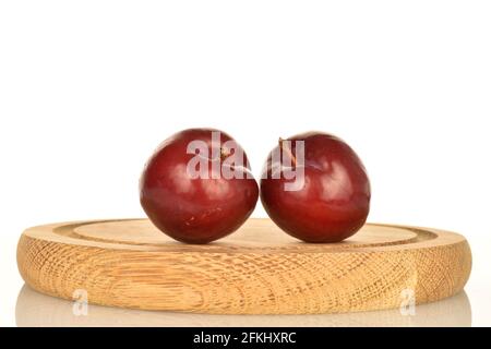 Two fresh juicy, organic red plums on a tray of wood, close-up, against a white background. Stock Photo