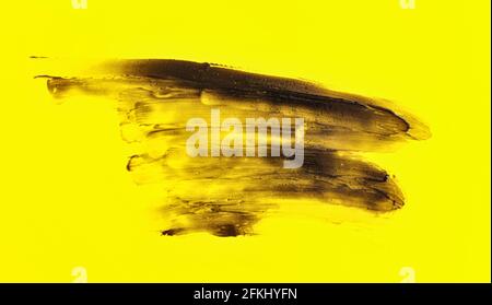 Black smears charcoal toothpaste over yellow board, abstract background Stock Photo