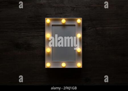 Glowing white frame with light bulbs on a vintage wooden background. Blank for postrer or postcards. Stock Photo