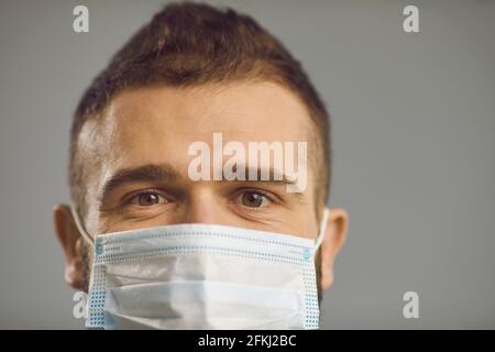 Eyes of a Caucasian millennial guy who is wearing a protective medical mask on a gray background. Stock Photo