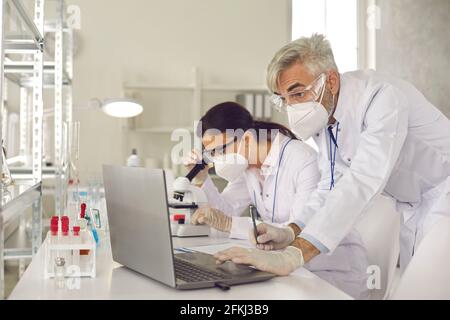 Microbiologist biotechnology researcher in facial mask conducting experiment Stock Photo