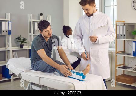 Young man with ankle injury complaining to doctor about pain and uncomfortable brace Stock Photo
