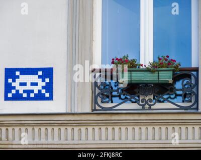 Street art in blue white, work of space invader in Paris on a facade of a historical building with a french balcony and flowers in city center. Stock Photo