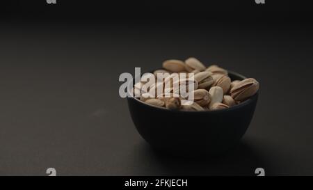 salted large pistachios in black bowl on black paper background, wide photo Stock Photo