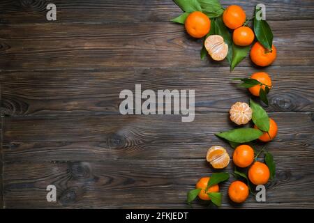 Bunch of fresh mandarin oranges, whole, halved & peeled, with leaves, on a dark brown wooden textured table. Healthy vegan vegetarian citrus food, vit Stock Photo