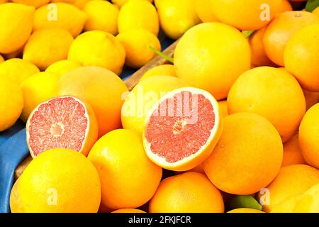 Harvest heap of fresh ripe organic yellow and red grapefruits on sunlight at local produce farmers market. Pile of citrus halved and whole. Clean eati Stock Photo