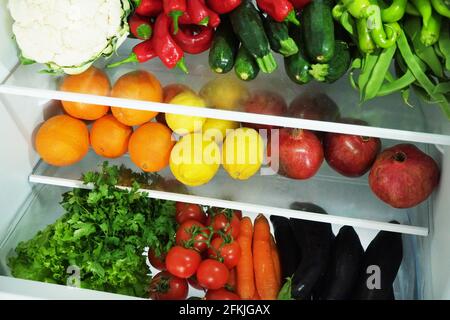 Stacked fridge full of fresh organic fruits and vegetables: orange, lemon, pomegranate, eggplant, carrot, parsley, pepper, cucumber, cauliflower, toma Stock Photo