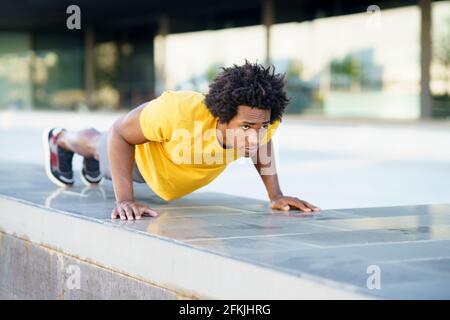 Black man doing triceps dip exercise on city street bench. Stock Photo