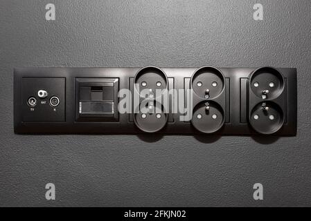 Black frame with electric, internet, TV and satellite sockets connected together on the black wall. Stock Photo