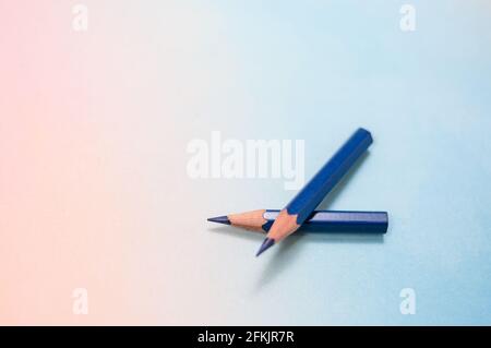 Rainbow-colored background, with two individual, blue colored pencils that are crossed. Large text field Stock Photo