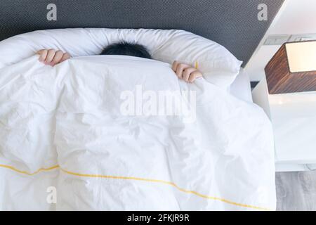 Lazy boy covering his face with blanket while lying in bed at home, Lazy to wake up concept Stock Photo