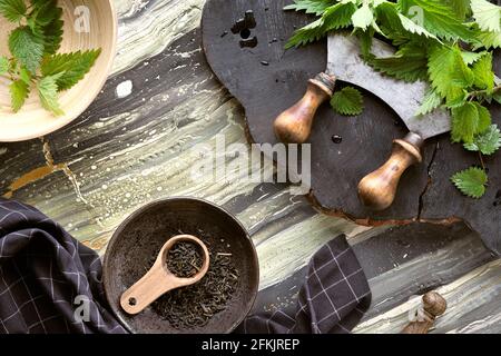 Stinging nettle, fresh herbs, herb knife on rustic wooden board. Dry nettle herb, herbal tea in wooden plate with scoop. Top view, flat lay. Stock Photo