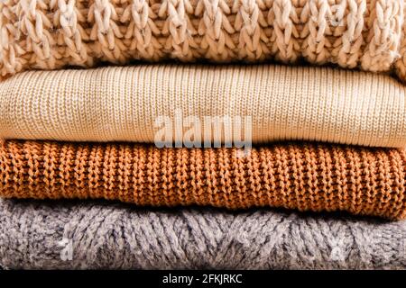 Bunch of knitted warm pastel color sweaters with different knitting patterns folded in stack, clearly visible texture. Stylish fall / winter season kn Stock Photo