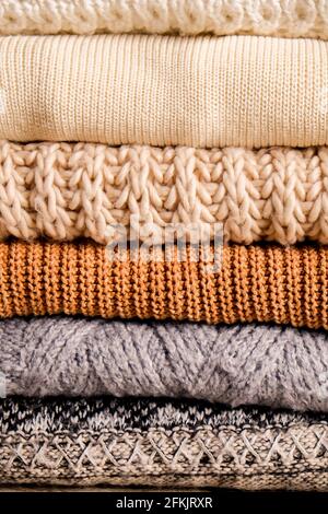 Bunch of knitted warm pastel color sweaters with different knitting patterns folded in stack, clearly visible texture. Stylish fall / winter season kn Stock Photo