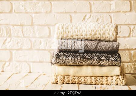 Bunch of knitted warm pastel color sweaters with different knitting patterns folded in stack on brown wooden table, grunged texture wall background. F Stock Photo