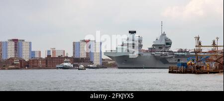 Portsmouth, England, UK. 2021. HMS Queen Elizabeth an aircraft carrier  with escorting tugs departs Portsmouth Harbour passing the colourful apartment Stock Photo