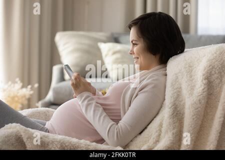 Smiling pregnant woman relax at home using smartphone Stock Photo