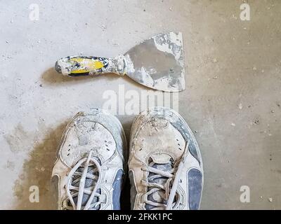 Old dirty work boots and a putty knife on cement floor - view from above Stock Photo