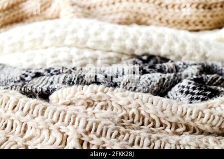 Bunch of knitted warm pastel color sweaters with different knitting patterns laid in messy pile, clearly visible texture. Stylish fall / winter season Stock Photo
