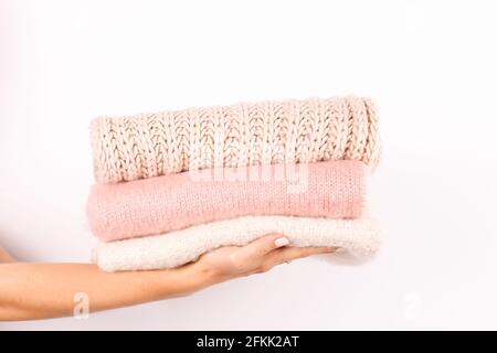 Close up of young woman holding huge stack of folded knitted warm pastel color sweaters, easy chic style, different knitting patterns. Light pink mani Stock Photo