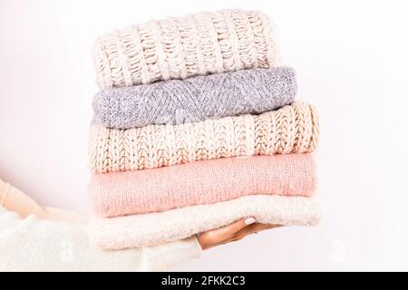 Close up of young woman holding huge stack of folded knitted warm pastel color sweaters, easy chic style, different knitting patterns. Light pink mani Stock Photo