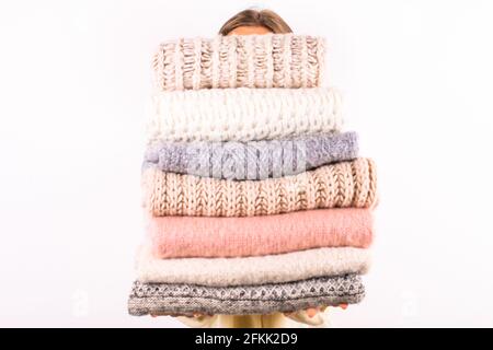 Close up of young woman holding huge stack of folded knitted warm pastel color sweaters, easy chic style, different knitting patterns. Light pink mani Stock Photo
