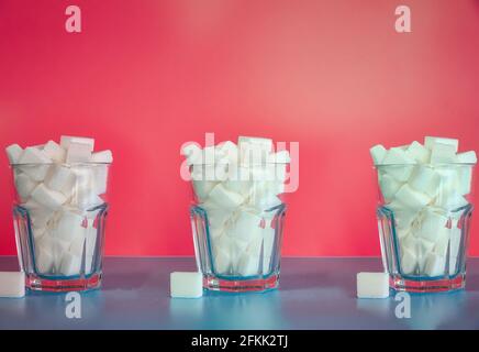 Three Glasses full with sugar cubes on pink background, sugar,unhealthy,sweets,junk food concept background retro modern design Stock Photo
