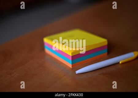 A pack of multicolored papers and a white pencil on a wooden board. Notepad with outlined colored sheets, white ballpoint pen on wooden table top. Rea Stock Photo