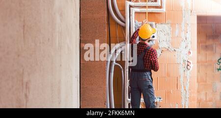 Male builder measuring the pipe attach on wall at construction site Stock Photo