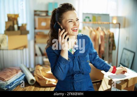 smiling 40 years old small business owner woman with clipboard talking on a smartphone in the office. Stock Photo