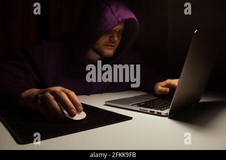 man in hoddie working on laptop till night dark background lamp light Stock Photo