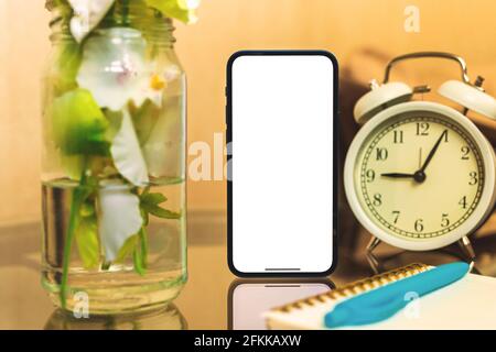 Mobile phone mockup, morning workspace home interior concept with flowers and alarm clock, copy space Stock Photo