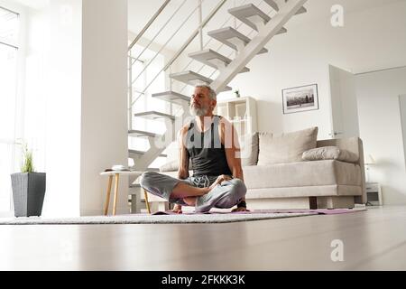 Strong older mid aged tattooed yogi man doing yoga exercises at home. Stock Photo