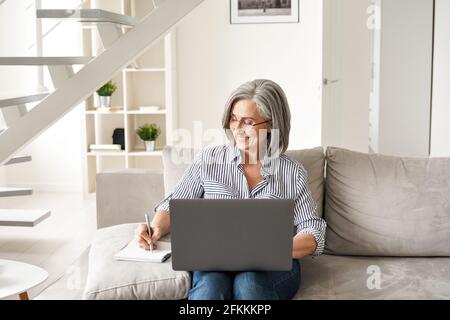 Happy mature old professional woman working on laptop from home office. Stock Photo